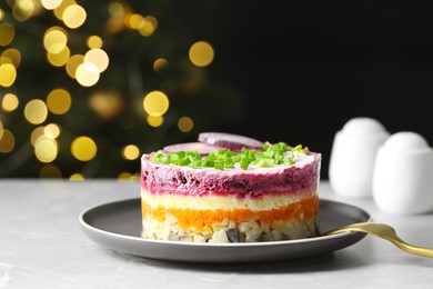 Photo of Herring under fur coat salad served on light grey table against blurred festive lights, space for text. Traditional Russian dish