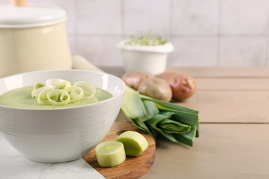 Photo of Tasty leek soup in bowl and fresh ingredients on wooden table, space for text