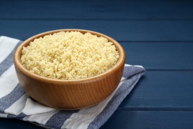 Photo of Bowl of tasty couscous on blue wooden table, closeup. Space for text