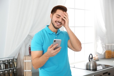 Photo of Young man laughing while using smartphone at home