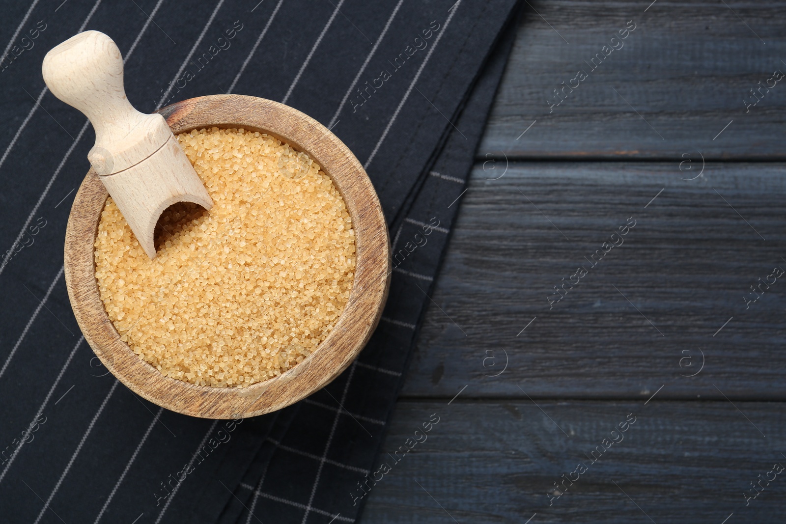 Photo of Brown sugar in bowl and scoop on black wooden table, top view. Space for text