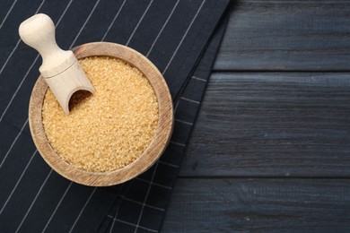 Photo of Brown sugar in bowl and scoop on black wooden table, top view. Space for text