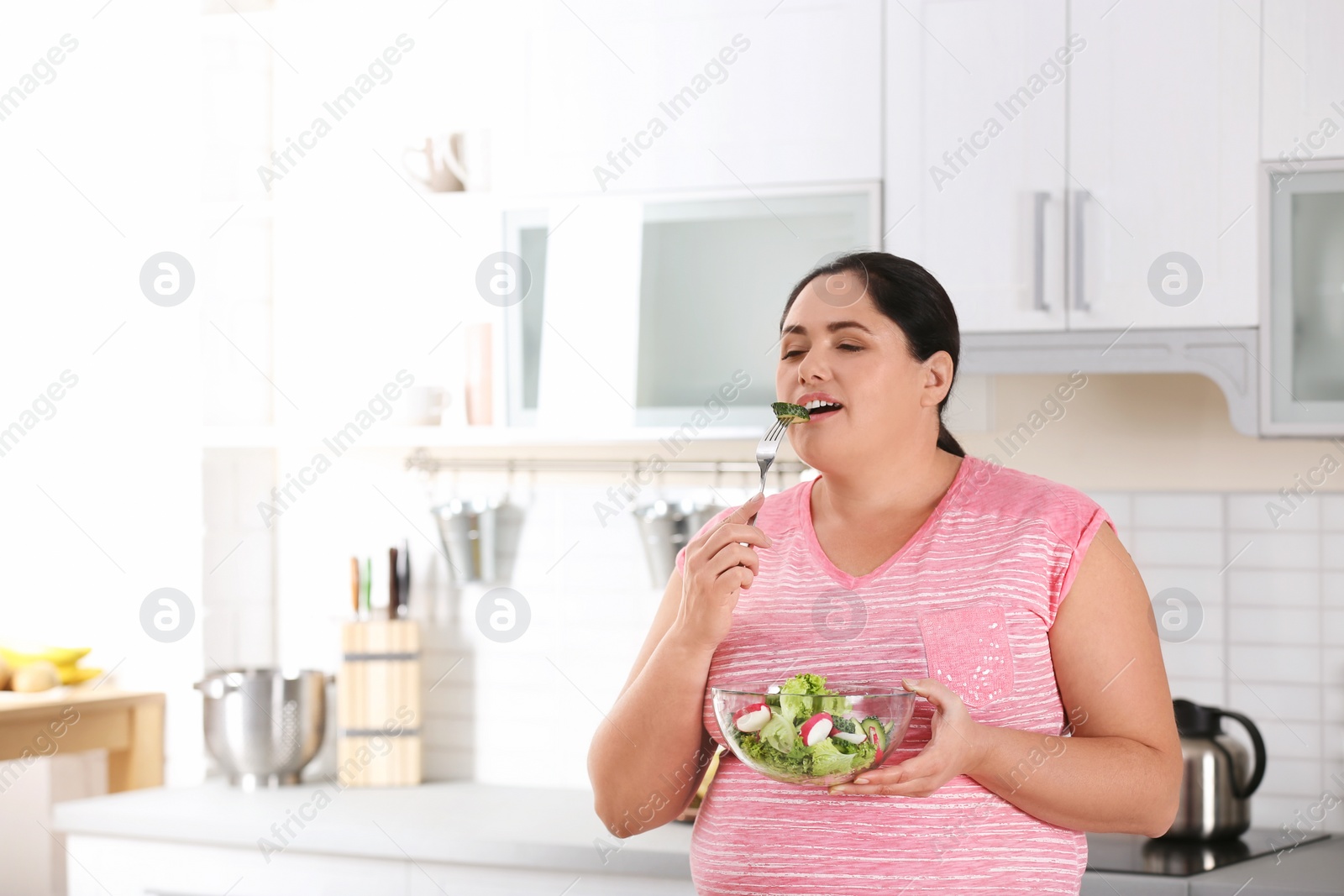 Photo of Woman eating vegetable salad in kitchen. Healthy diet