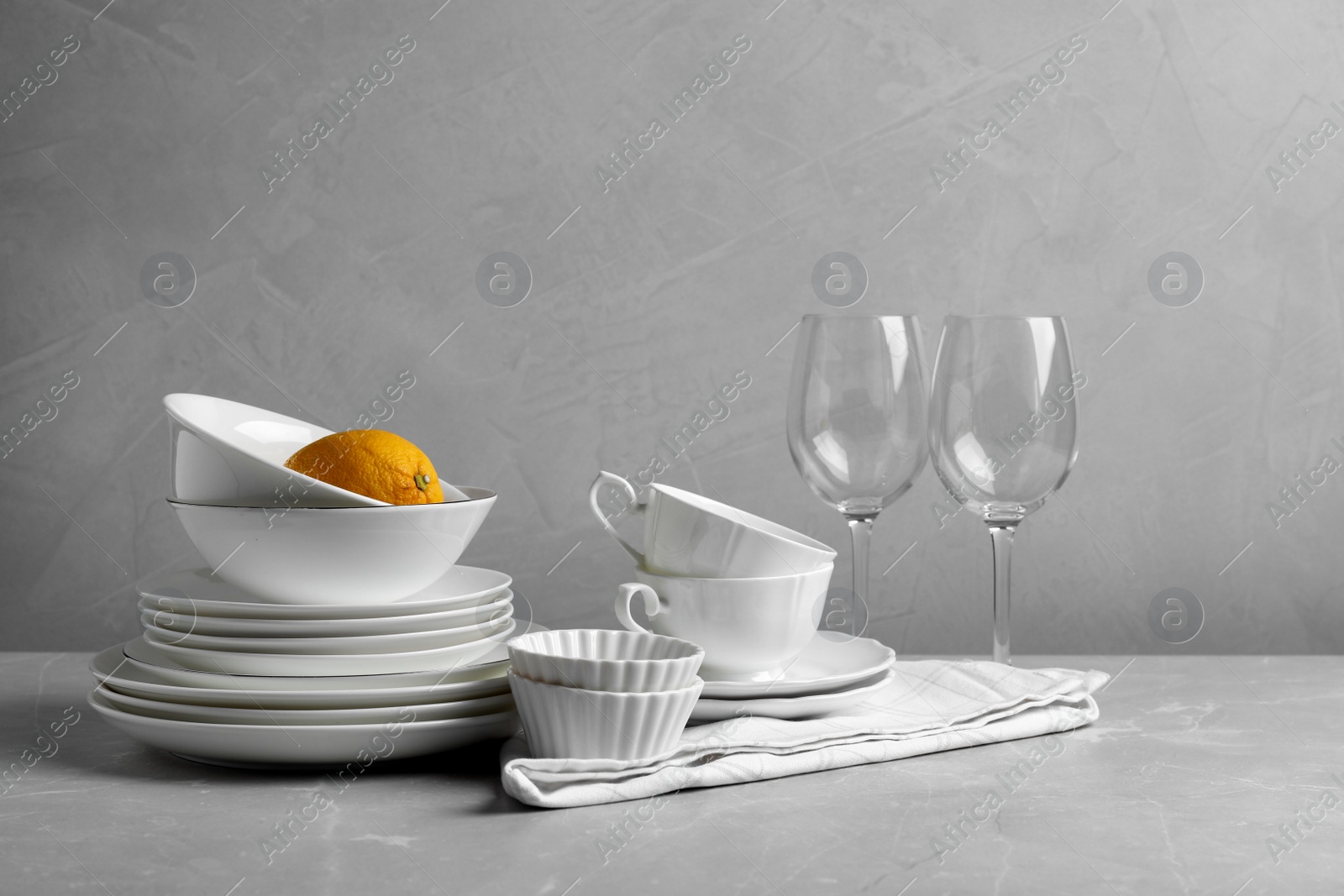 Photo of Set of clean dishware, glasses and lemon on light grey table