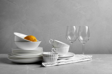 Set of clean dishware, glasses and lemon on light grey table