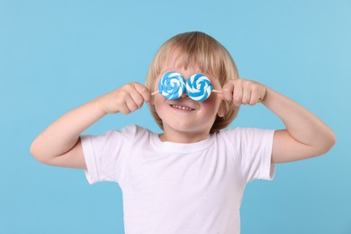 Little boy covering his eyes with bright lollipops on light blue background