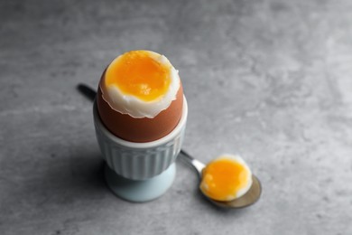 Photo of Fresh soft boiled egg in cup on grey table. Space for text