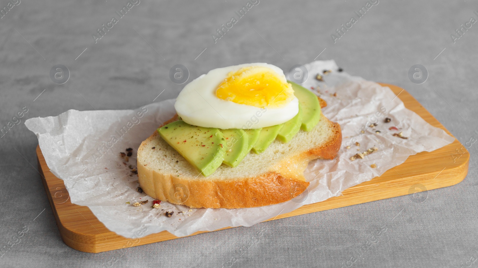 Photo of Delicious sandwich with boiled egg and pieces of avocado on gray table