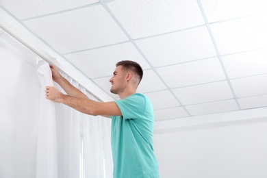 Man hanging window curtain indoors. Interior decor element