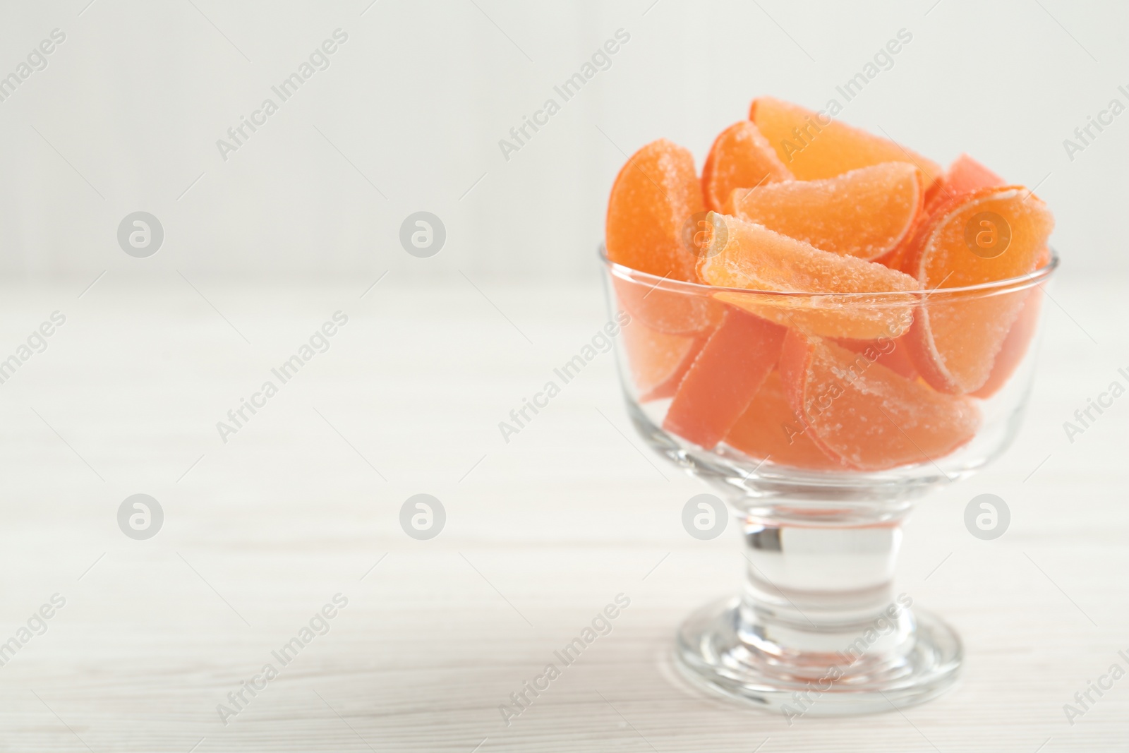 Photo of Tasty orange jelly candies in glass dessert bowl on white wooden table. Space for text