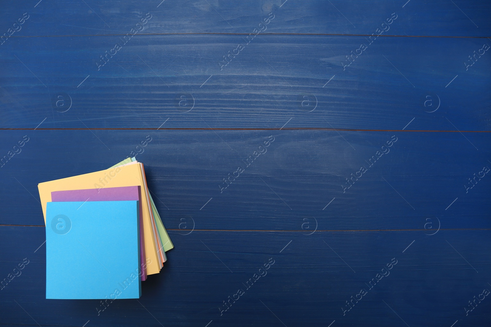 Photo of Stack of colorful stickers on blue wooden table, top view. Space for text