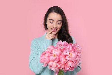 Beautiful young woman with bouquet of peonies on pink background