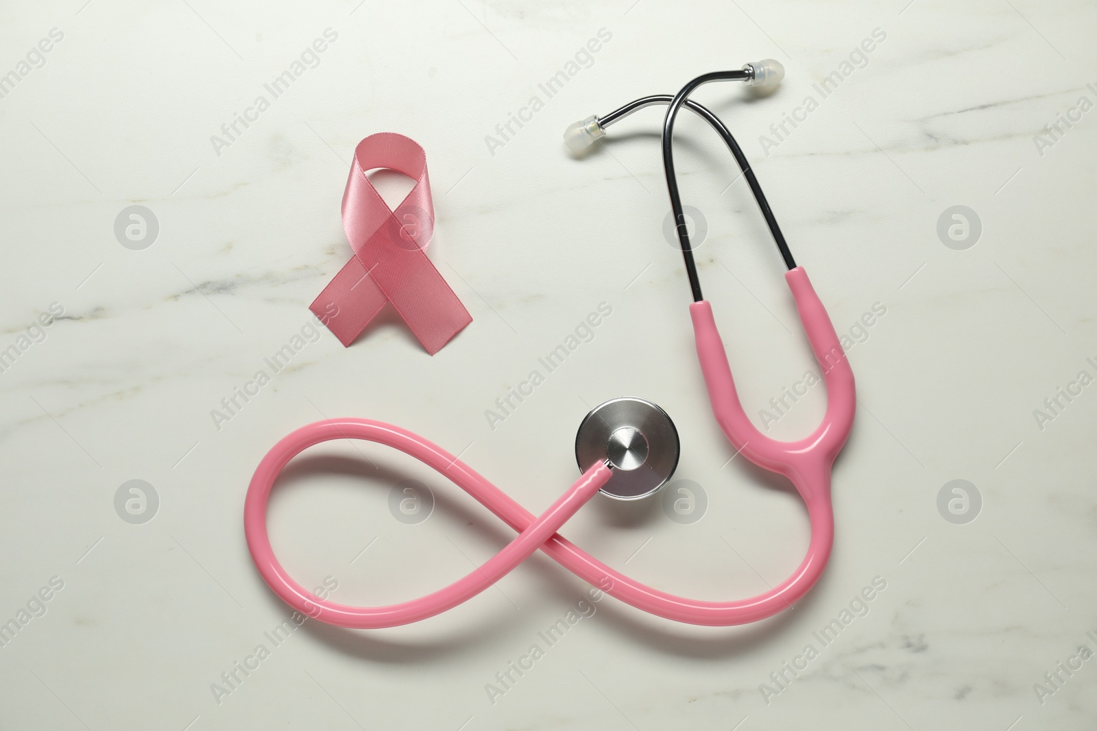 Photo of Pink ribbon and stethoscope on white marble table, flat lay. Breast cancer awareness