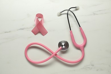 Pink ribbon and stethoscope on white marble table, flat lay. Breast cancer awareness