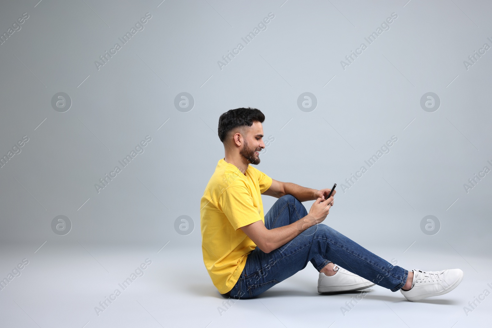 Photo of Happy young man using smartphone on grey background, space for text