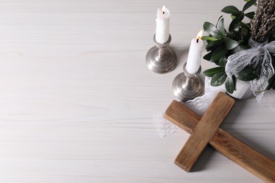 Burning candles, bouquet with willow branches and cross on white wooden table, flat lay. Space for text