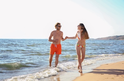 Happy young couple in beachwear spending time together on seashore