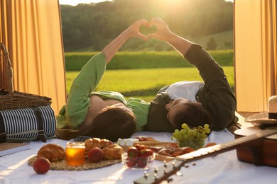Romantic date. Couple making heart with hands during picnic on sunny day