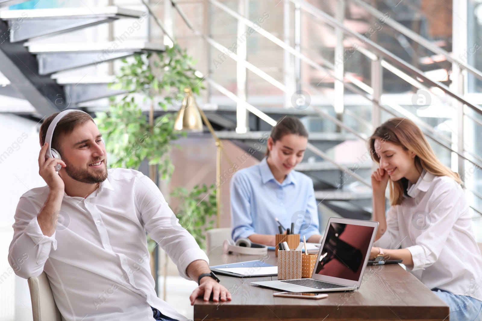 Photo of Young businessman with headphones, laptop and his colleagues at table in office