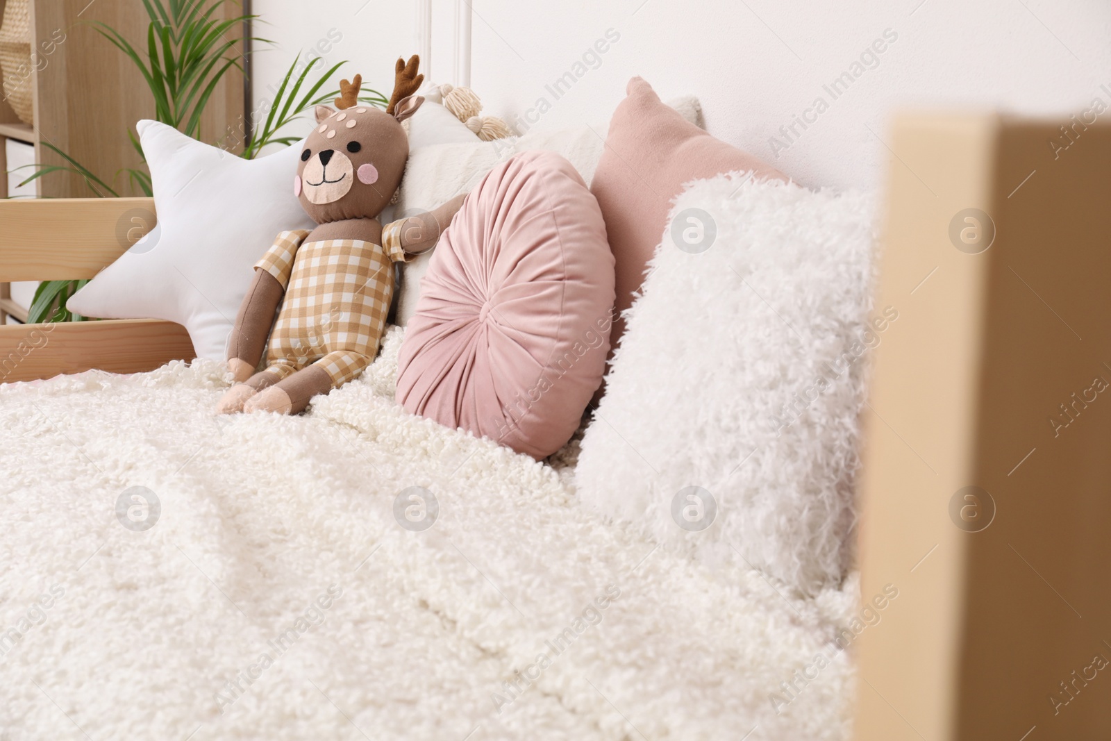 Photo of Comfortable bed with pillows and toy deer in child's room. Interior design