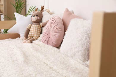 Photo of Comfortable bed with pillows and toy deer in child's room. Interior design