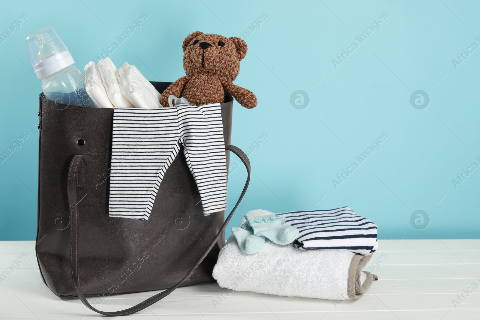 Photo of Mother's bag with baby's stuff on white wooden table against light blue background