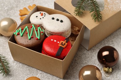 Photo of Tasty Christmas macarons in box and festive decor on table, closeup