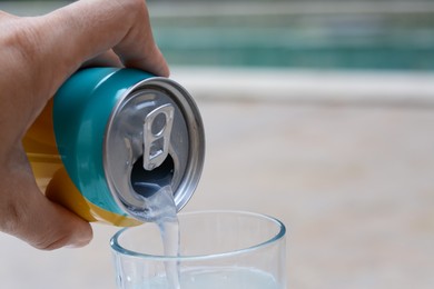 Photo of Woman pouring drink from aluminum can into glass on blurred background, closeup. Space for text