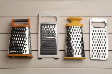 Different modern graters on white wooden table, flat lay