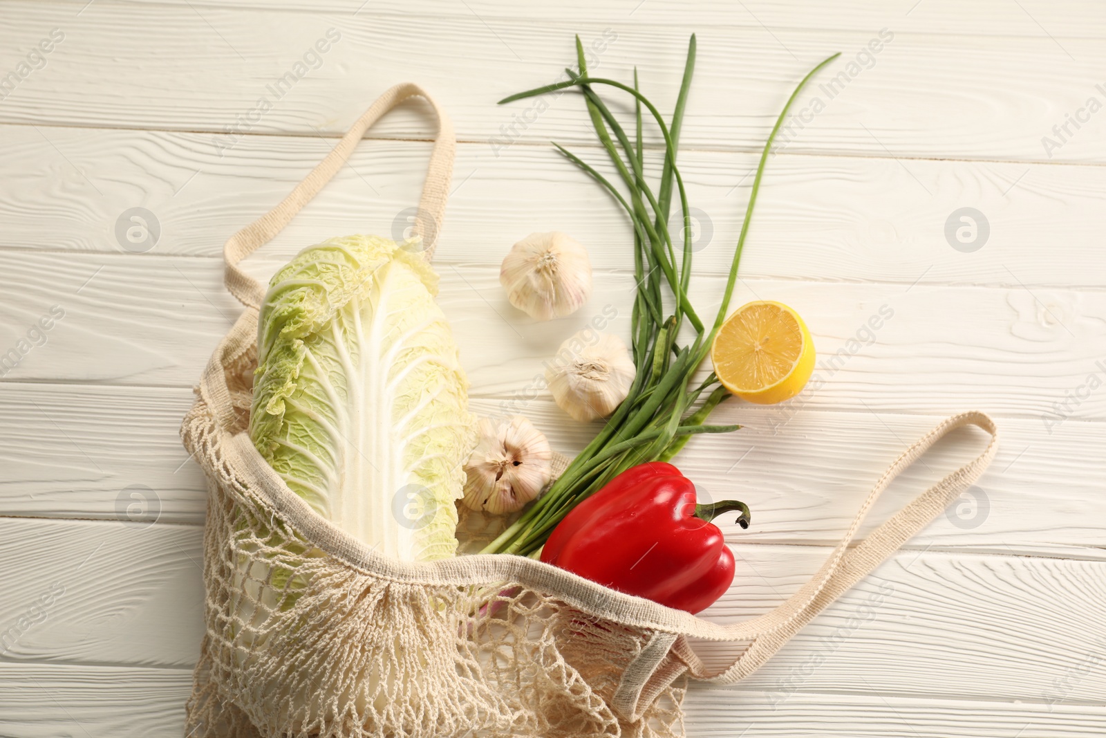 Photo of Fresh ripe Chinese cabbage and other vegetables in net bag on white wooden table, top view