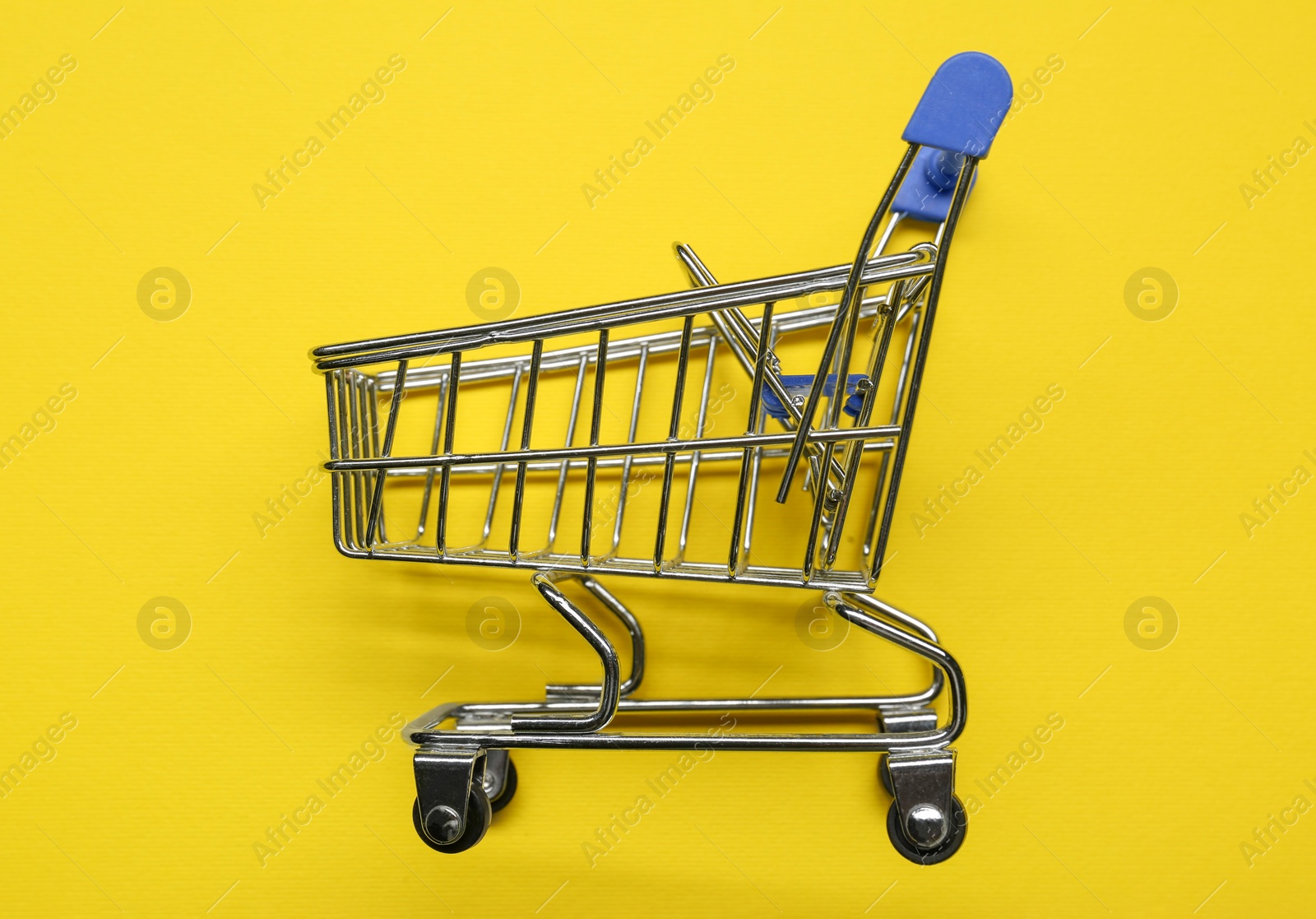 Photo of Small metal shopping cart on yellow background, top view