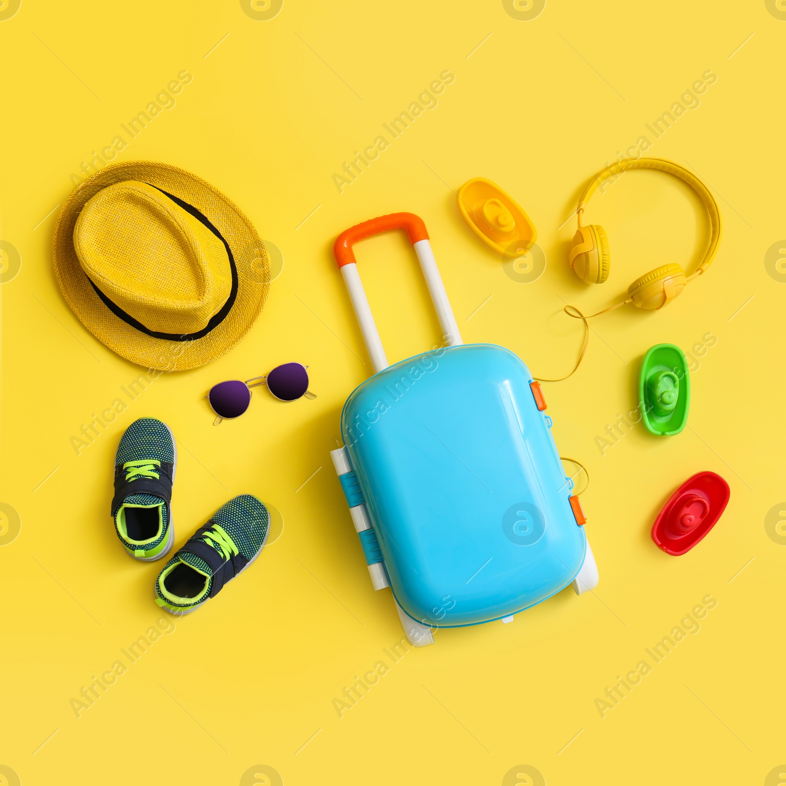 Photo of Flat lay composition with blue suitcase and child accessories on yellow background. Summer vacation