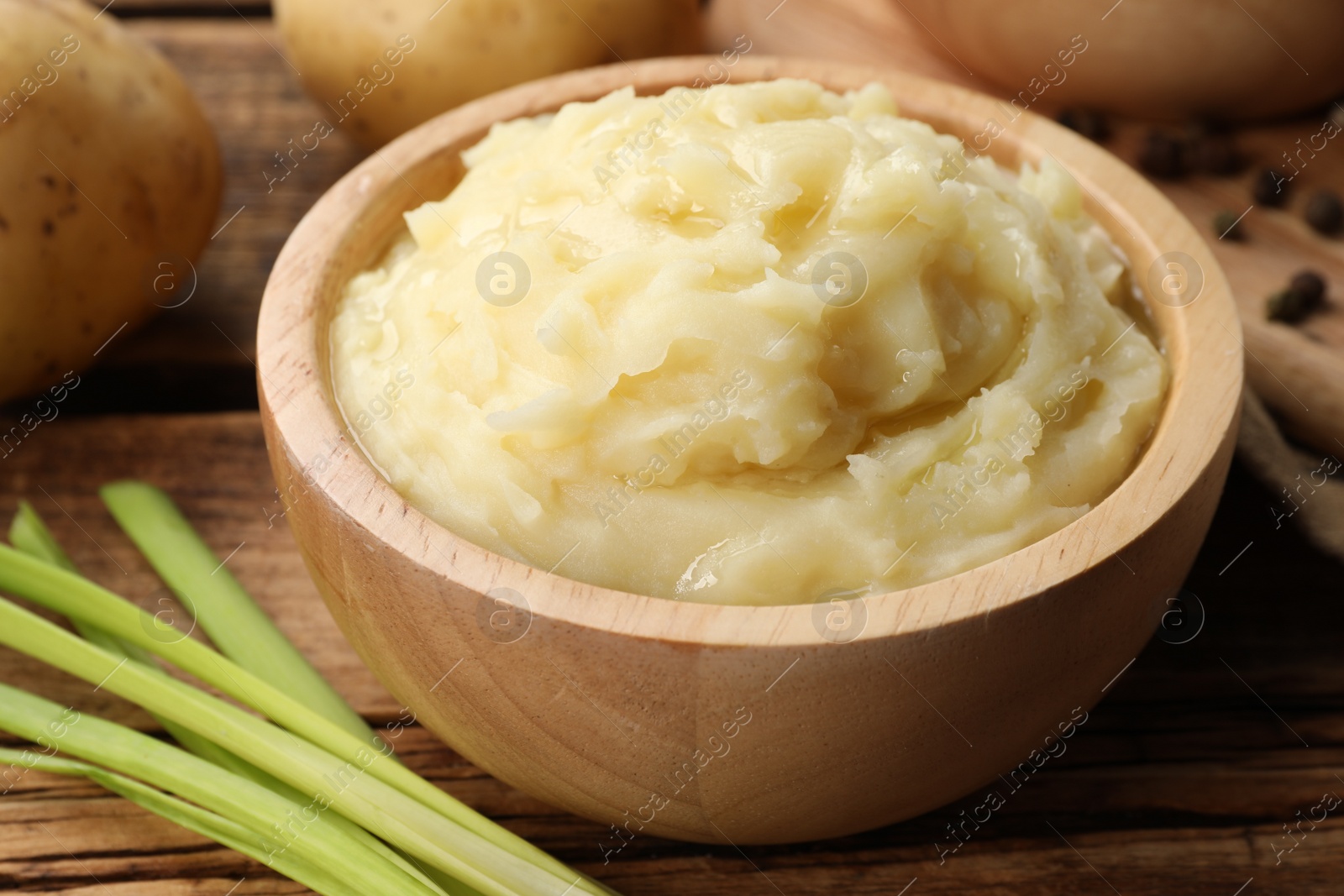 Photo of Bowl of tasty mashed potato, pepper and leeks on wooden table, closeup