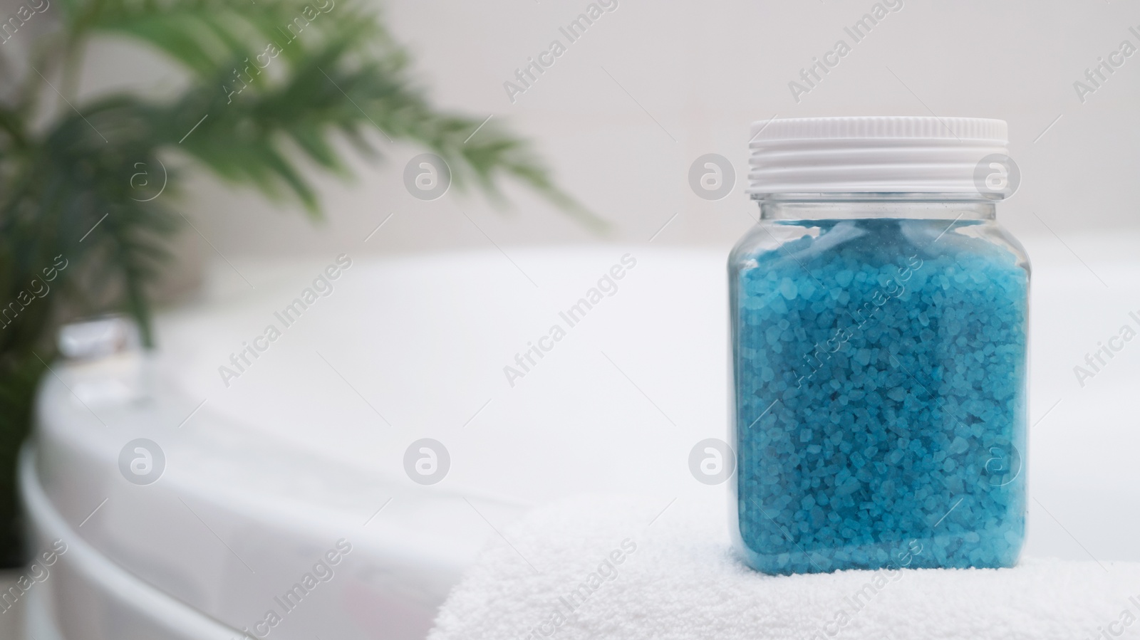 Jar with sea salt and fluffy towel on bath. Space for text Photo of Jar with sea salt and fluffy towel on bath. Space for text