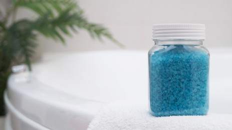 Photo of Jar with sea salt and fluffy towel on bath. Space for text