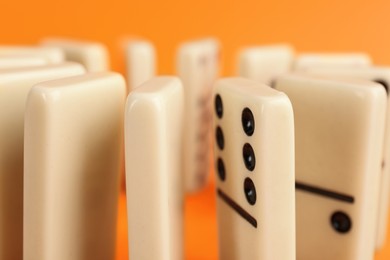 Photo of White domino tiles with black pips on orange background, closeup