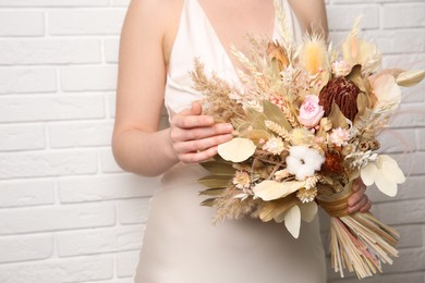 Photo of Bride holding beautiful dried flower bouquet near white brick wall, closeup