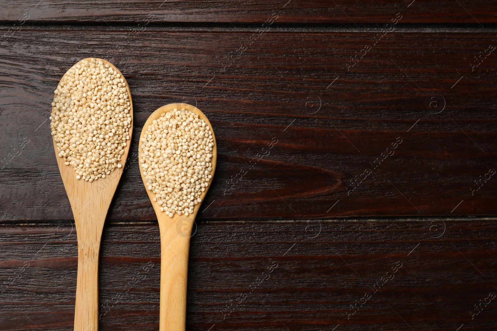 Photo of Spoons with dry quinoa seeds on wooden table, flat lay. Space for text