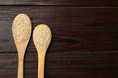 Photo of Spoons with dry quinoa seeds on wooden table, flat lay. Space for text