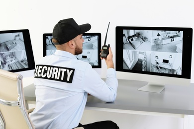 Photo of Male security guard with portable transmitter monitoring home cameras indoors
