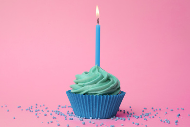 Photo of Delicious birthday cupcake with turquoise cream and burning candle on pink background