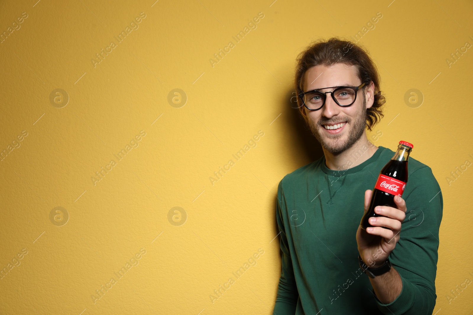 Photo of MYKOLAIV, UKRAINE - NOVEMBER 28, 2018: Young man with bottle of Coca-Cola on color background, space for text