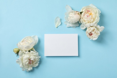 Fresh peonies and empty card on color background, flat lay with space for text