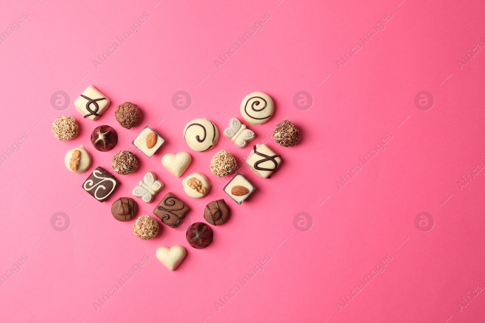 Photo of Heart made with delicious chocolate candies on pink background, top view. Space for text