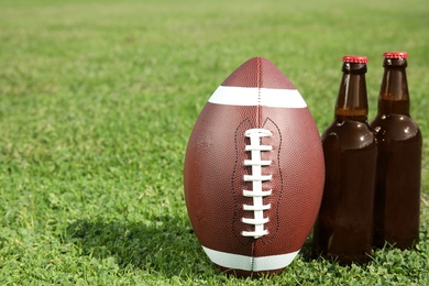 Photo of Ball for American football and beverage on fresh green field grass. Space for text