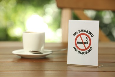 Photo of No Smoking sign and cup of drink on wooden table outdoors. Space for text