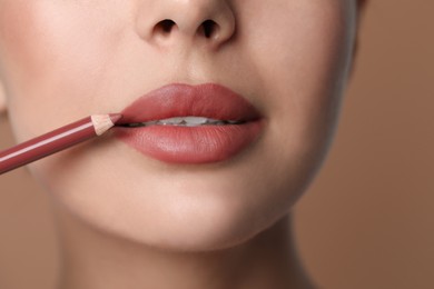 Photo of Young woman applying beautiful nude lip pencil on brown background, closeup