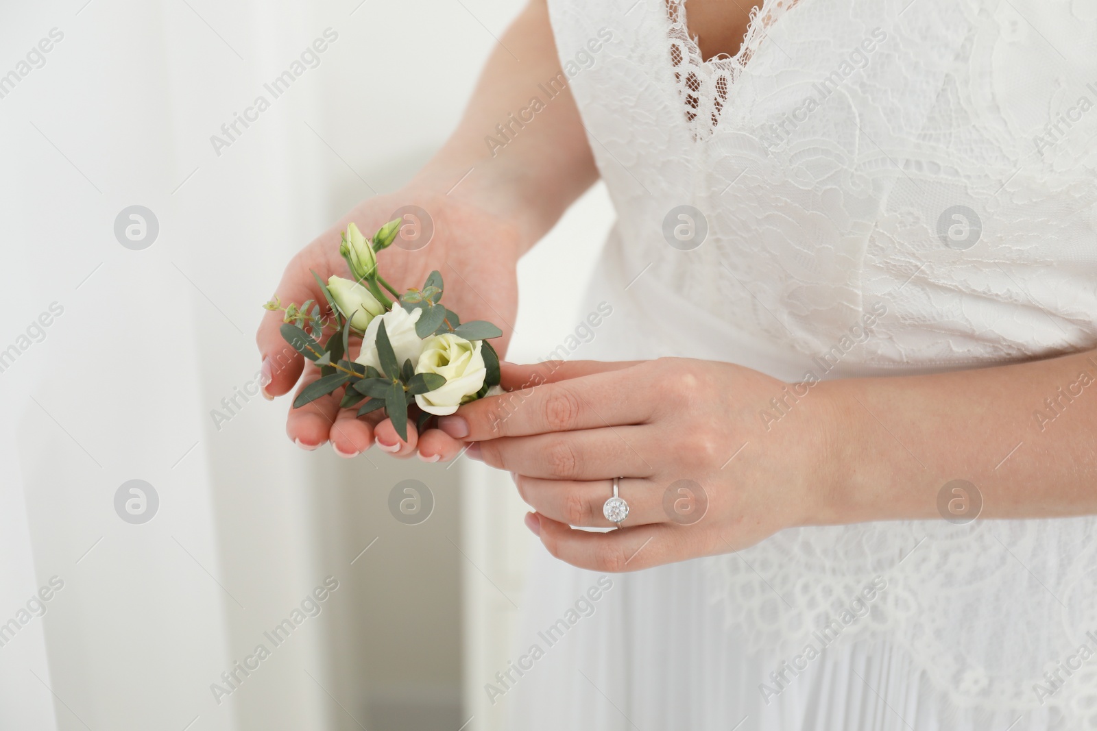 Photo of Bride holding boutonniere for her groom on blurred background, closeup