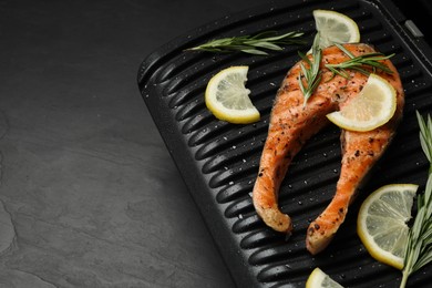 Photo of Cooking salmon. Grill with tasty fish steak, lemon and rosemary on grey table. Space for text