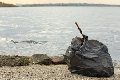 Photo of Trash bag full of garbage on beach. Space for text